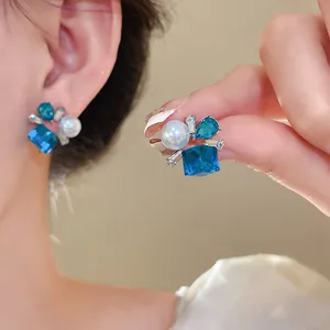 Vista macro de pendientes de botón con cristal azul y perla con finos detalles plateados