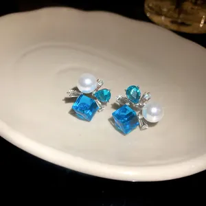 Vista detallada de pendientes de plata con cristales azules cuadrados y perlas redondas.