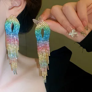 Dettaglio ravvicinato di orecchini a nappa con strass sfumati colorati indossati da una modella.