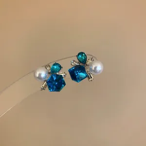 Primer plano de pendientes geométricos de cristal azul y perlas con base de plata