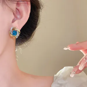 Imagen de detalle de un elegante pendiente dorado con una gema azul cuadrada