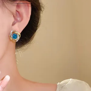 Primer plano detallado de pendientes dorados con una piedra cuadrada azul y pequeños cristales