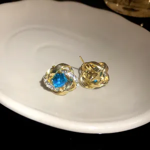 Vista detallada de pendientes de nudo de oro con una piedra de circonita azul cuadrada