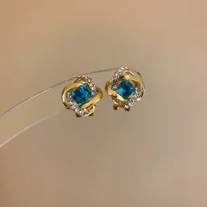 Detalle de pendientes de nudo dorados con cristal azul cuadrado y detalles brillantes