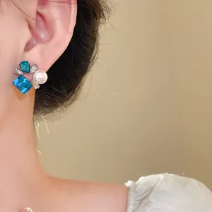 Primer plano de un elegante pendiente de cristal azul y perla blanca en la oreja