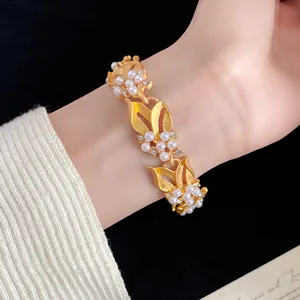 Nahaufnahme eines goldenen Weizenblatt-Armbands mit Perlen und Zirkonia am Handgelenk.