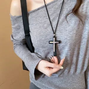 Detail shot of a vintage leather double cross pendant necklace worn over a grey sweater.