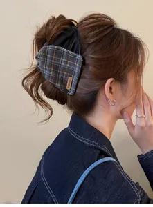 Detailed view of a vintage plaid and leather large hair claw clip worn on styled brown hair.