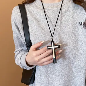 Detailed close-up of large dual-layered cross pendant necklace with black cord on model