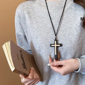 Close-up detail of retro double cross pendant on black cord worn by model with book