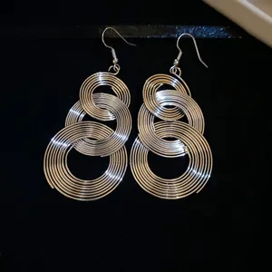 Close-up detail of silver tiered concentric circle dangle earrings on black surface.