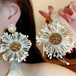Detail of raffia flower earrings with gold hammered metal center and white petals.