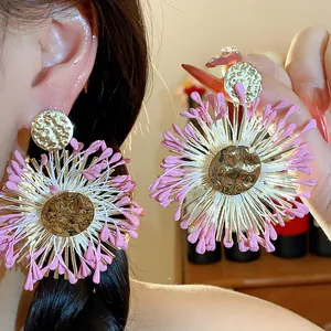 Close-up of pink and white raffia flower earrings with gold textured centers