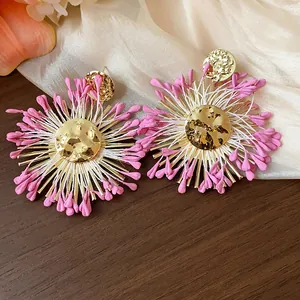 Macro view of oversized raffia flower earrings with hammered gold metal and pink accents