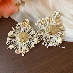 Exquisite macro detail of bohemian raffia flower stud earrings with gold metallic centers.
