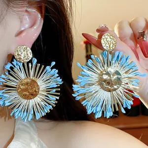 Detailed macro view of blue raffia flower earrings with hammered gold sunburst design