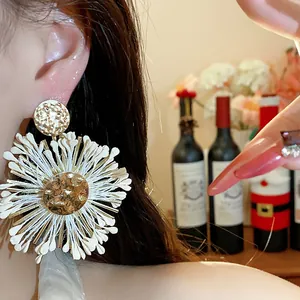 Close-up of handmade raffia flower earrings with metallic hammered gold center detail.