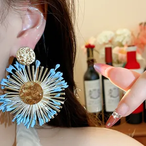 Close-up detail of blue raffia flower earring with gold accents worn by an Asian model