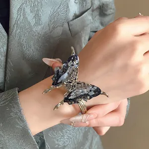 Detailed view of a silver butterfly open bracelet with blue textured wings on a hand.