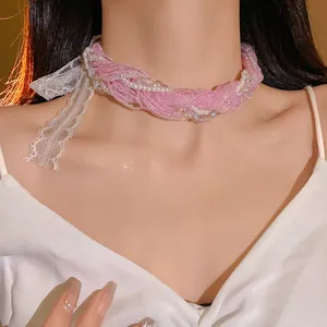 Dettaglio di un choker con perline rosa decorato con un fiocco di pizzo bianco e perle