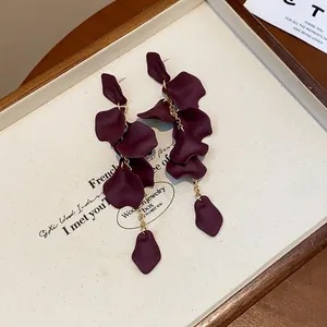 Primo piano dei ciondoli a petalo rosso scuro opaco su lunghi orecchini pendenti stile vintage.