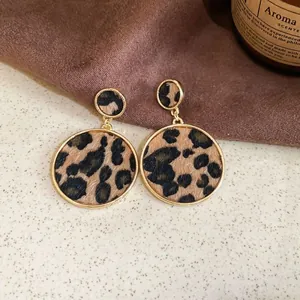 Gros plan de boucles d'oreilles rondes rétro imprimé léopard avec bordure dorée sur tissu marron.