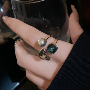 Close-up detail of an adjustable gold-plated ring featuring a pearl and green gemstones.