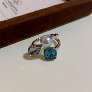Close-up of an open ring featuring a pearl, blue square crystal, and grey pear stone.