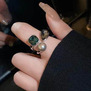 Close-up detail of vintage open ring featuring a grey pearl and square green gemstones.