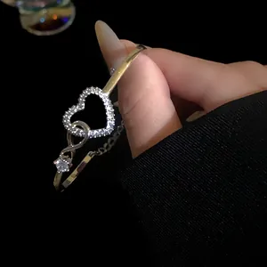 Close-up of elegant golden bangle with zircon-paved hollow heart and infinity charm
