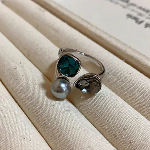 Detailed close-up of a vintage open ring featuring a teal crystal, gray pearl, and brown stone