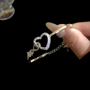 Close-up of golden open bangle bracelet featuring a hollow heart set with zircon stones