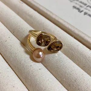 Detailed macro view of a gold plated open ring featuring brown crystals and a pearl