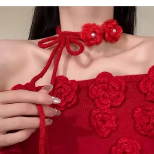 Détail d'un collier ras du cou en fleurs tricotées rouges avec des accents de perles