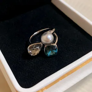Close-up of a vintage style open ring featuring a pearl and blue crystal in a box.