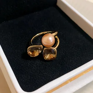 Close-up of a gold-plated open ring with a pearl and brown faceted gemstones