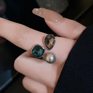 Detailed view of an open ring featuring teal crystal, smoky gem, and grey pearl