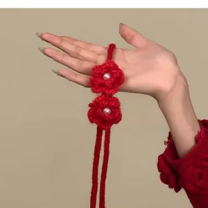 Détail d'un collier de fleurs tricotées rouges avec perle blanche tenu à la main