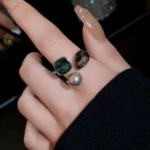 Detailed view of an open ring with emerald crystal, teardrop stone, and grey pearl.
