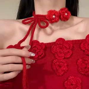 Gros plan d'un ras-du-cou en tricot rouge avec des détails de fleurs et de perles.
