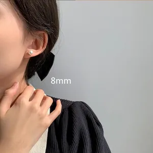 Detalle de pendientes de botón con perla blanca redonda de 8mm y aguja de plata en modelo