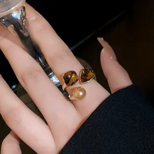 Close-up of elegant retro gold-plated ring with brown gems and pearl on female finger