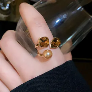 Close-up of gold-plated open ring featuring a pearl and amber-colored crystals on a finger.