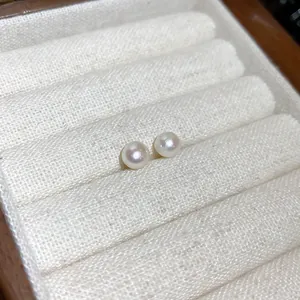 Primer plano de elegantes pendientes de perlas redondas en un joyero de tela blanca