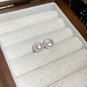 Primer plano de elegantes pendientes de perlas redondas en un joyero de madera de lujo.