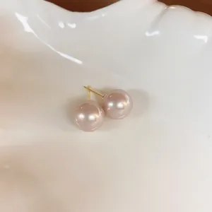 Detalle macro de elegantes pendientes de perlas rosa champán en superficie crema