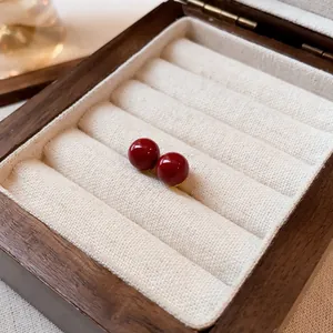 Primer plano de elegantes pendientes de bola roja en un joyero de madera rústico