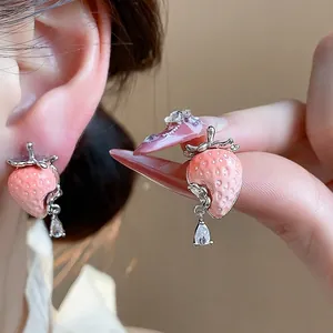 Eleganti orecchini a fragola in resina rosa con goccia di zircone indossati e in mano