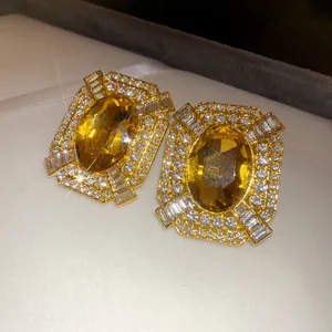 Primo piano di orecchini vintage rettangolari in oro con grande gemma gialla e cristalli.