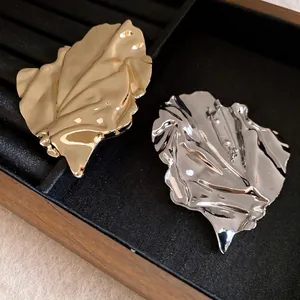Elegant gold and silver irregular crumpled metal leaf brooches displayed on black felt